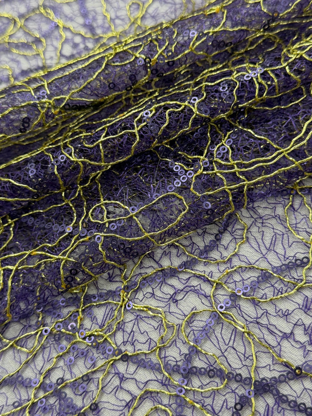 Close-up of a sheer tulle fabric with a purple base and an intricate overlay of gold sequins and mesh.